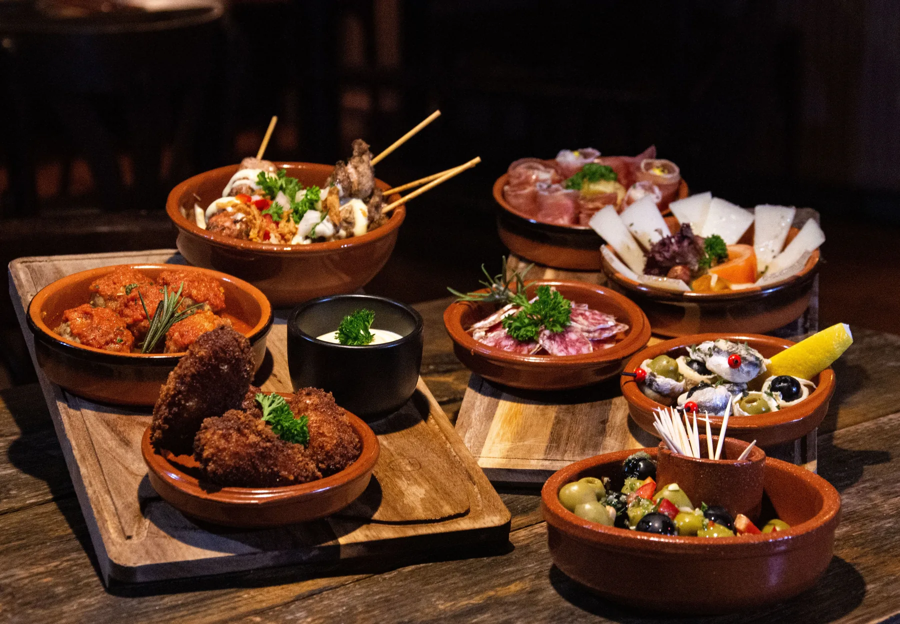 Small clay dishes of tapas laid out on a dark wooden table
